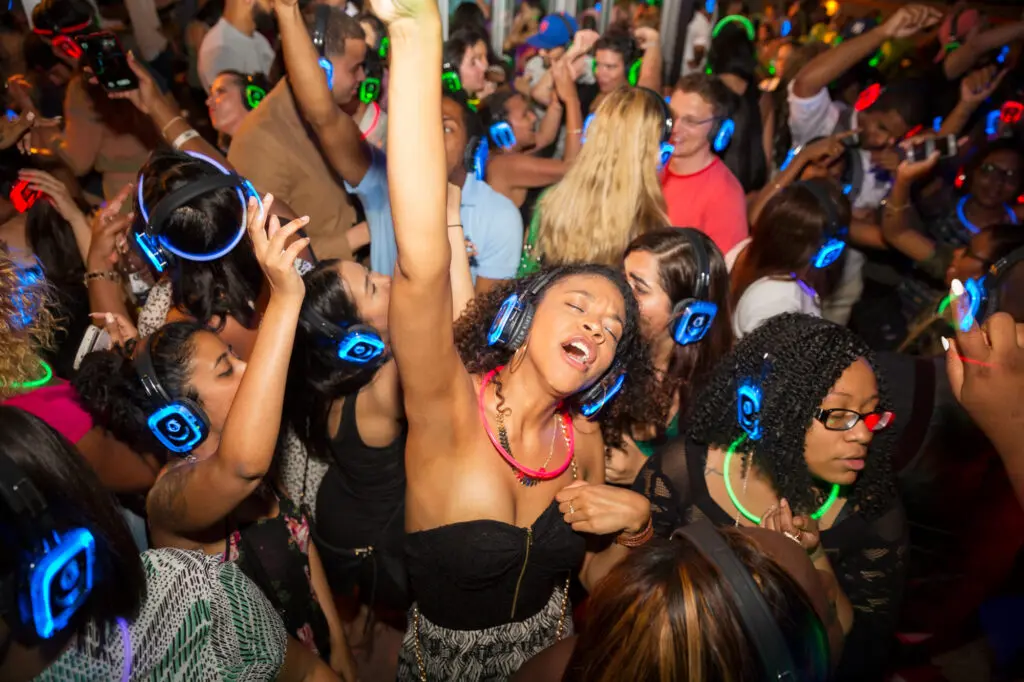 A crowded group wears glowing headphones, dancing and celebrating at a silent disco party without disturbing neighbors.